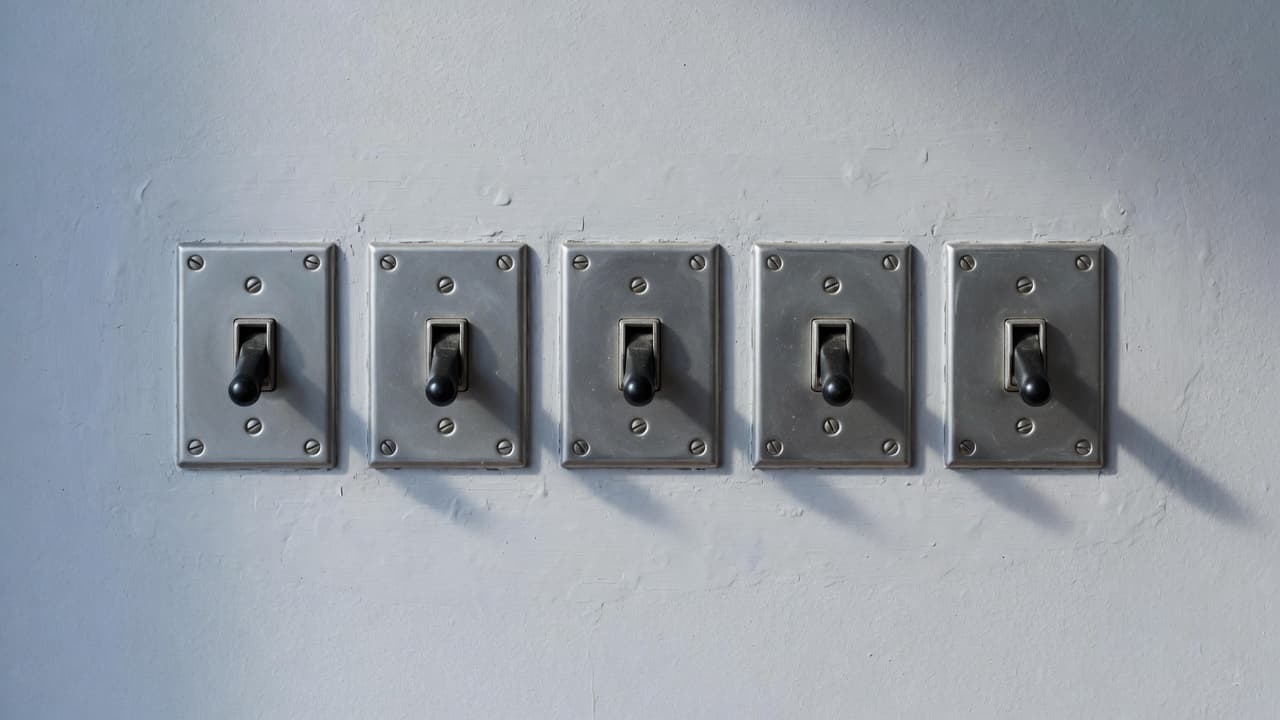 Five metal toggle switches in a row on a pale wall.